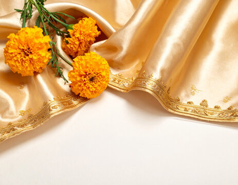 Draped Golden Silk Saree with Zari Border and Fresh Marigold Flowers Background