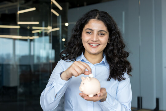 Young woman saving money in piggy bank at office