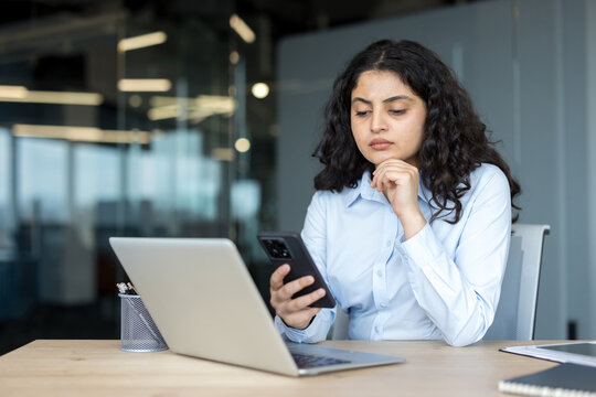 Professional woman using smartphone and laptop in office