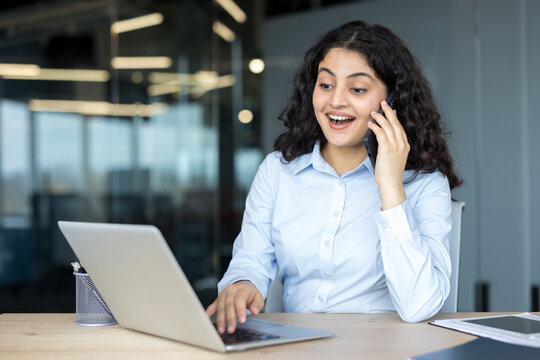 Excited young woman talking on smartphone working on laptop