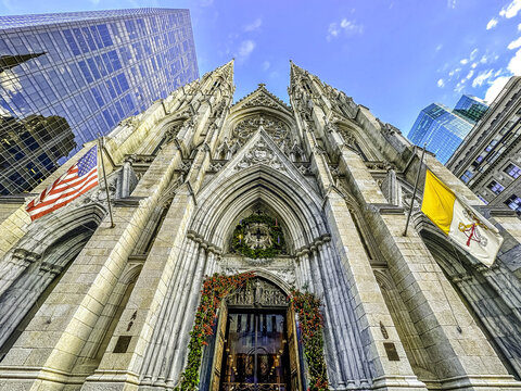 New York, United States - 28 November 2022: View of the neo-Gothic facade of St. Patrick's Cathedral on Fifth Avenue, decorated with holiday wreaths and flags under a blue sky.