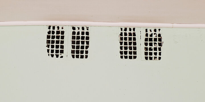 Weathered ventilation grilles with chipped paint against a pale green wall, suggesting wear and lack of maintenance