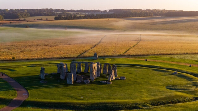 Aerial view of the prehistoric monument Stonehenge surrounded by lush green fields and morning mist in the English countryside near Salisbury, England, United Kingdom.