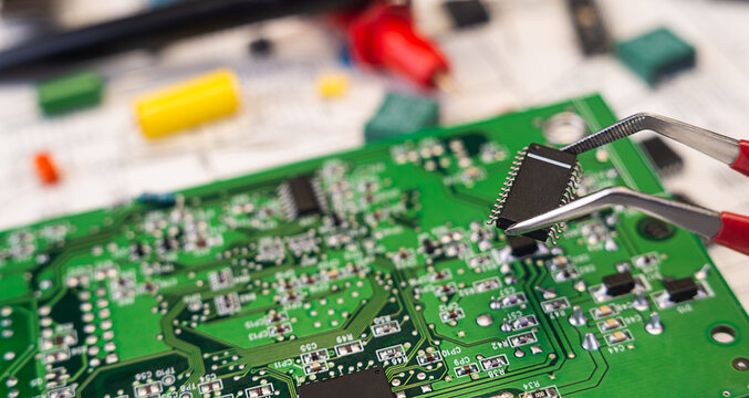 Working on a circuit board with tools in a workshop, focusing on a chip installation process