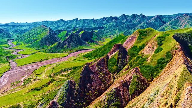 High angle view of dramatic green mountains and winding river valley in Xinjiang Danxia landform under clear blue sky.