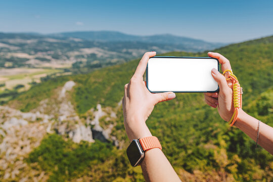 Mountain valley overlook framed by hands holding a smartphone with blank white screen mockup. Travel app concept.