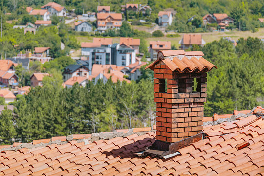 Brick chimney centered on terracotta tile roof with residential hillside village in background. Real estate concept.