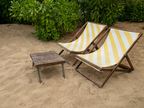 Yellow striped beach deck chairs and wooden table on sand