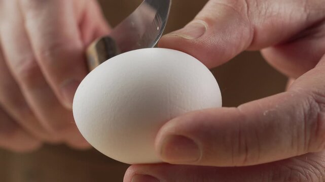 A close-up of a man's hands using a knife to crack a whole egg. The concept is protein nutrition and baking