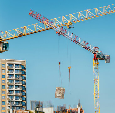 Two tower cranes building a modern apartment complex and new city infrastructure against a clear blue sky