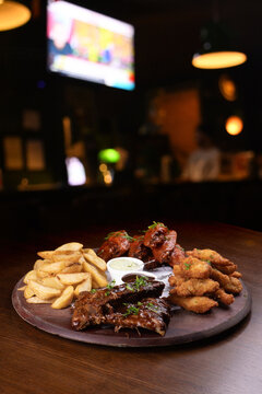 Tapas and finger food board featuring BBQ ribs, fried chicken, french fries, and buffalo wings, set on a table with a blurred background.