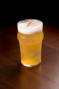 Half-pint glass of Radler beer with ice on a wooden table.