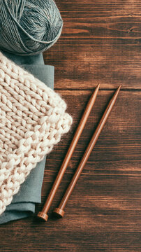 Cream chunky knit sweater with wooden knitting needle and gray yarn on rustic wood surface