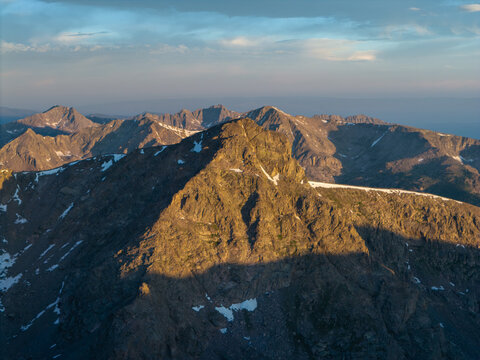 Aerial view of the rugged Mount of the Holy Cross in the Sawatch Range, featuring rocky peaks, lingering snow patches, and warm golden hour light in Vail, Colorado, United States.