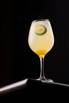 Limoncello spritz glass isolated on a wooden table, low-angle shot against a black background, with lemon and gin.