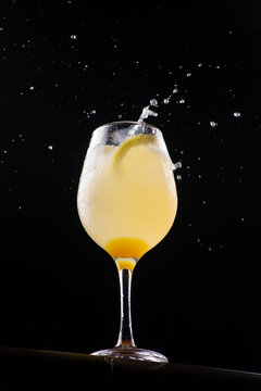Limoncello glass with a splash, low-angle shot, black background.