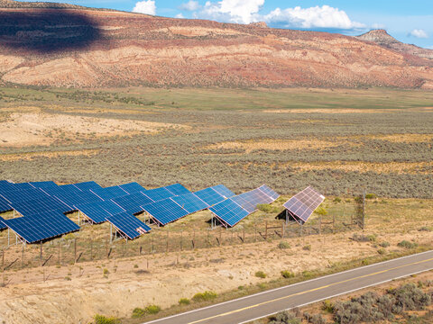 Aerial view of a solar farm with rows of photovoltaic panels installed in an arid desert landscape with mesas in the background and a road in the foreground in Colorado, United States.
