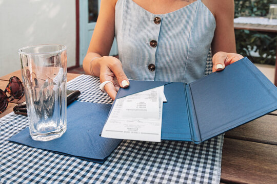 Woman's hands holding a blue folder with a paper receipt, preparing to pay for a meal at an outdoor restaurant