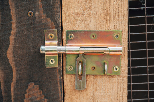 Metal bolt lock providing security and protection on a wooden gate, featuring mesh wire in the background
