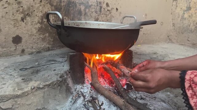 A villager woman adds wood fuel to a outside brick cooking stove with naked flames,Pakistan 