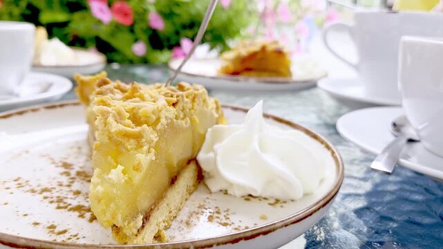 apple crumb pie slice with whipped cream on ceramic plate, surrounded by tea cups and garden flowers at an outdoor afternoon table setting