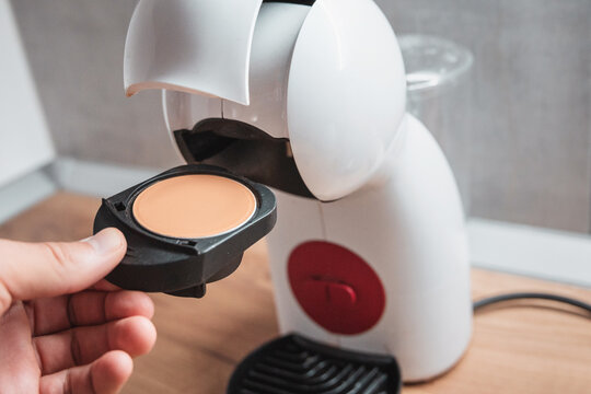 Hand holding coffee pod capsule with open pod coffee machine on wooden table. Home brewing concept.