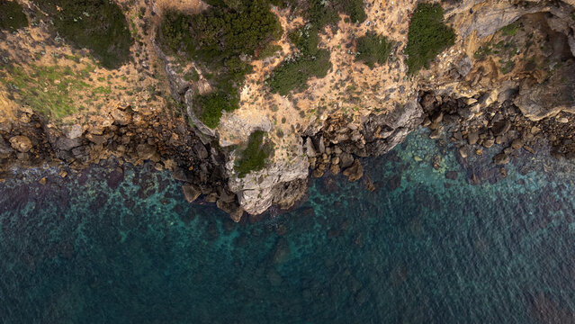 Aerial view of Cala Sarraina featuring rugged cliffs, rocky shoreline, and clear turquoise sea water in Trinita d'Agultu e Vignola, Sardinia, Italy.