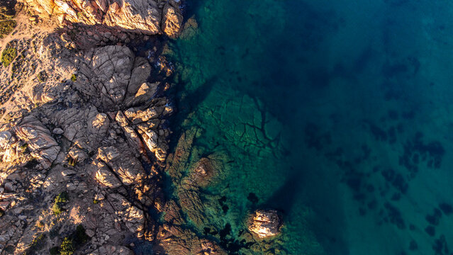 Aerial view of Cala Sarraina featuring rugged granite cliffs and turquoise waters illuminated by golden hour light in Trinita d'Agultu e Vignola, Sardinia, Italy.
