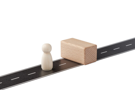 Business obstacle concept with wooden figure facing a barrier on road.