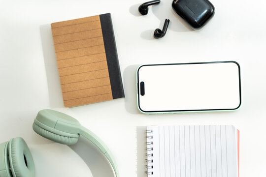 Smartphone with headphones and notebooks on white desk