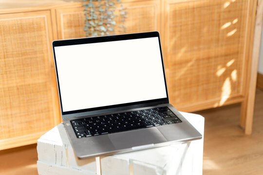 Laptop with blank white screen on wooden desk in sunlit interior