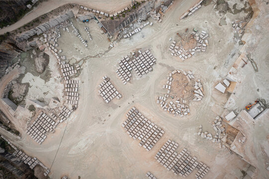 Aerial view of Cantera Porrino granite quarry with organized stacks of cut stone blocks, dusty ground, and heavy machinery in O Porrino, Pontevedra, Spain.