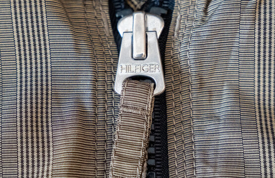 Warsaw, Poland - Sep 30, 2026: Close-up of a silver Tommy Hilfiger zipper pull hanging on a black zip of a glen check jacket, metal hardware detail with engraved Hilfiger lettering on beige plaid fab