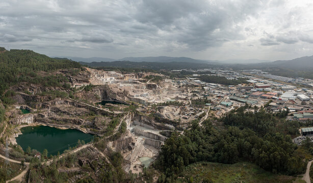 Aerial view of Cantera Porrino, a large granite quarry featuring deep green water pools, terraced stone extraction levels, and industrial infrastructure in O Porrino, Pontevedra, Spain.