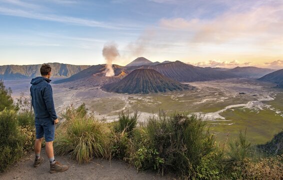 Young man in front of volcanic landscape at sunset, view in Tengger Caldera, smoking volcano Gunung Bromo, in front Mt. Batok, in the back Mt. Kursi, Mt. Gunung Semeru, National Park Bromo-Tengger-Semeru, Java, Indonesia