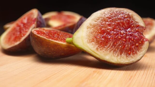 Macro shot captures ripe cut figs lying on wooden cutting board inside studio during smooth camera motion. Cinematic organic fruit video footage provides tasty textured asset for design element.
