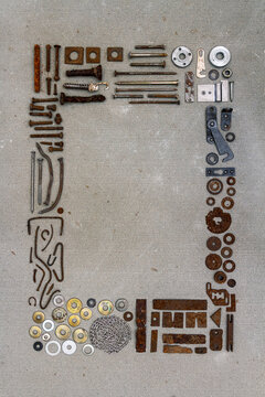 A frame of various old rusty bits and pieces arranged on a concrete surface. Old rusty nuts, bolts, nails and other parts flay lay on gray background.
