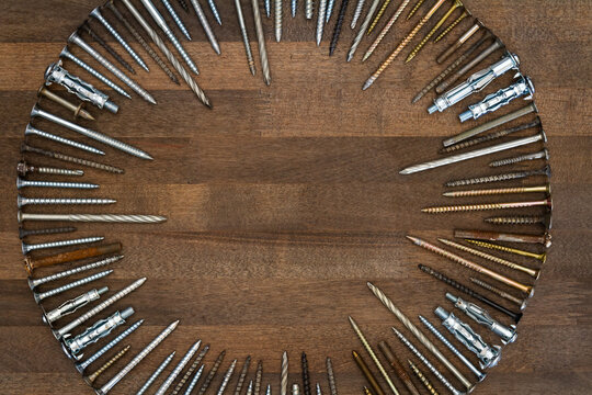 Circle made of various screws and nails on brown wood texture. Industrial flat lay. Carpentry still life.