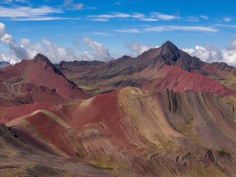Aerial view of Rainbow Mountain, also known as Vinicunca, featuring vibrant mineral-rich striped slopes under a blue sky with scattered clouds in the Peruvian Andes, Cusco, Cuzco, Peru.