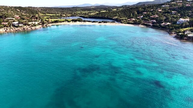 Fixed aerial view of Cala Girgolu in spring, showing the turquoise Mediterranean Sea, rocky coastline and surrounding natural landscape in Sardinia, Italy.