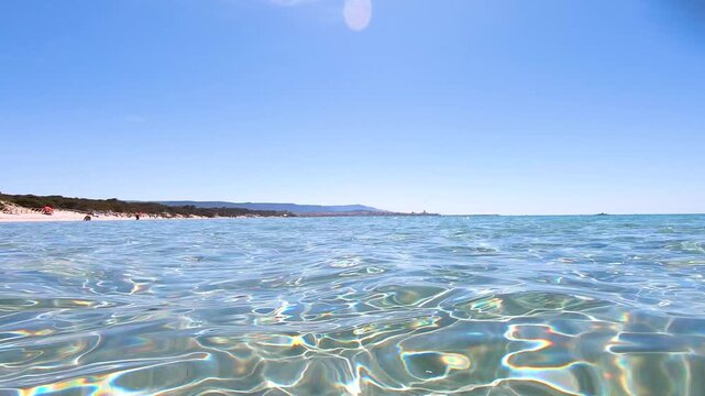 Slow motion view filmed at sea level of clear water at Maria Pia Beach, capturing gentle waves and the Mediterranean shoreline in Alghero, Sardinia.