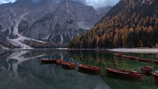 Aerial view of Pragser Wildsee featuring wooden boats moored on the calm lake surface surrounded by autumn foliage and dramatic mountain peaks in Prags, Trentino-Alto AdigeS, Italy.