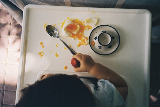 A little girl eating an egg that got smashed on the table