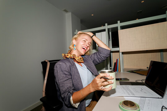 Woman Enjoying Coffee in Office While Laughing and Working