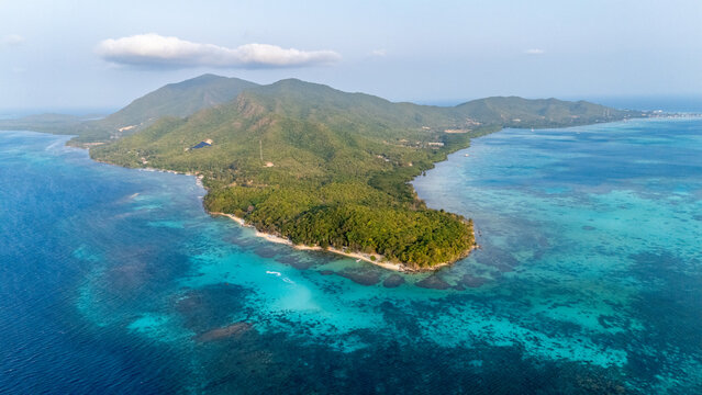 Aerial view of the lush green island of Karimunjawa surrounded by turquoise coral reefs and deep blue sea in Karimunjawa, Central Java, Indonesia.