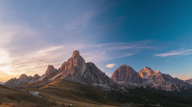 Time lapse of golden sunset light on Ra Gusela peak at Passo Giau, Dolomites, Italy. Shadows creep across an alpine meadow under a clear sky. Serenity, passing time and freedom in the mountains