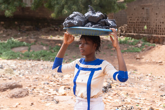Young African woman balances a tray of black market bags on her head outdoors, representing informal work, female entrepreneurship, livelihood and economic resilience