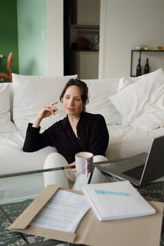 Woman Sitting on Couch With Laptop and Papers in Indoor Setting