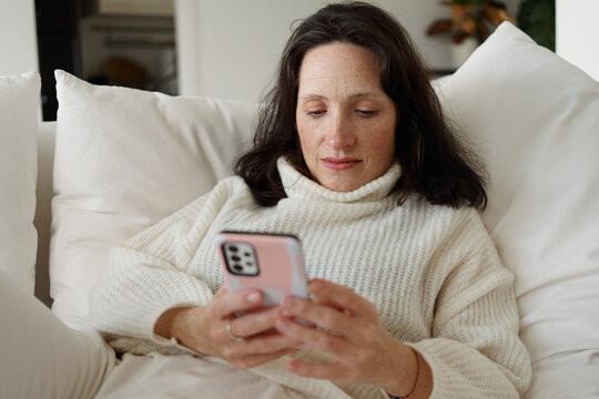 Woman Using Phone While Sitting on a Couch at Home