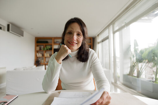 Woman Sitting at a Table in a Bright Room Smiling With Paperwork